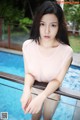 A woman in a pink shirt sitting by a swimming pool.