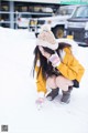 A woman crouching down in the snow with a pair of gloves on.