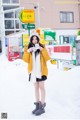 A woman standing in the snow in front of a parking lot.