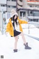 A woman in a yellow jacket and black skirt is standing in the snow.