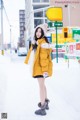 A woman in a yellow coat is standing in the snow.