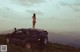 A naked woman standing on top of a car.