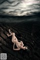 A naked woman laying on top of a dirt field.