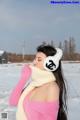 A woman in a pink sweater and white ear muffs in the snow.