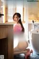 A woman in a pink sweater is posing in a bathroom.