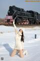 A woman in a white sweater and hat posing in front of a train.