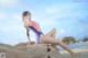 A woman in a bathing suit sitting on a rock on the beach.