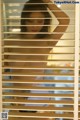 A naked woman standing in front of a window with blinds.