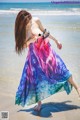 A woman in a colorful dress is walking on the beach.