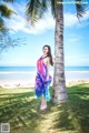 A woman standing next to a palm tree on the beach.