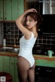 A woman in a white bodysuit standing in a kitchen.