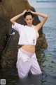 A woman in a white top and purple pants standing in the water.