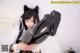 A woman in a black cat ears outfit is holding a pair of boots.