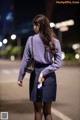 A woman in a purple shirt and blue skirt is walking down the street.