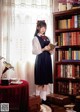 A woman standing in front of a book shelf holding a book.