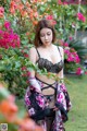 A woman in lingerie standing in front of a bush of flowers.