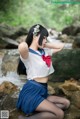 A woman in a school uniform sitting on a rock by a stream.