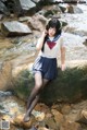 A woman in a sailor outfit sitting on a rock by a stream.