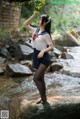 A woman in a school uniform standing on a rock by a stream.