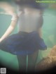 A woman in a white shirt and blue skirt is underwater.