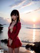 A woman in a red dress standing on a beach.