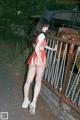 A woman in a red and white cheerleader outfit leaning against a fence.