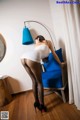 A woman in a white dress and black stockings leaning against a blue chair.