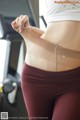 A woman in a white top and maroon leggings on a treadmill.